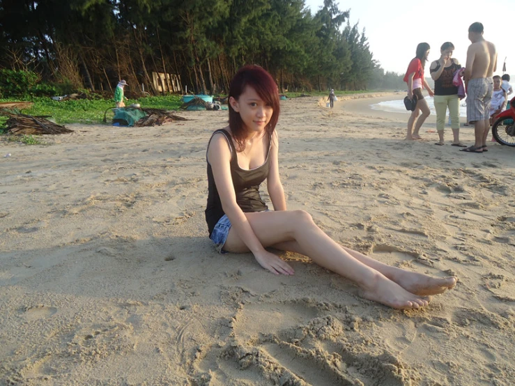 a woman with long legs and red hair sits on the sand of a beach