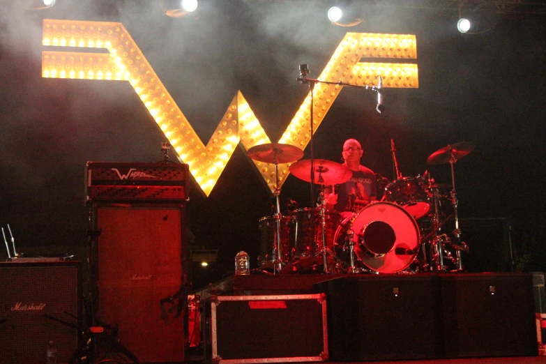 a man that is playing drums in front of some lights