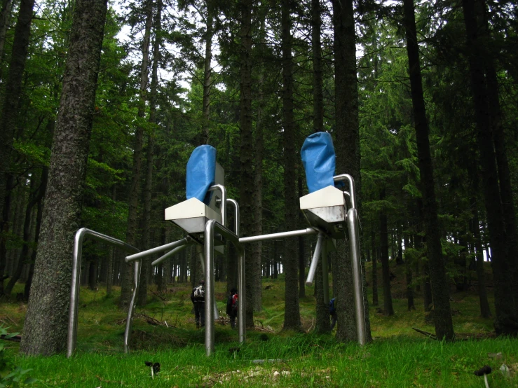 two outdoor toilets with blue covers sitting next to trees