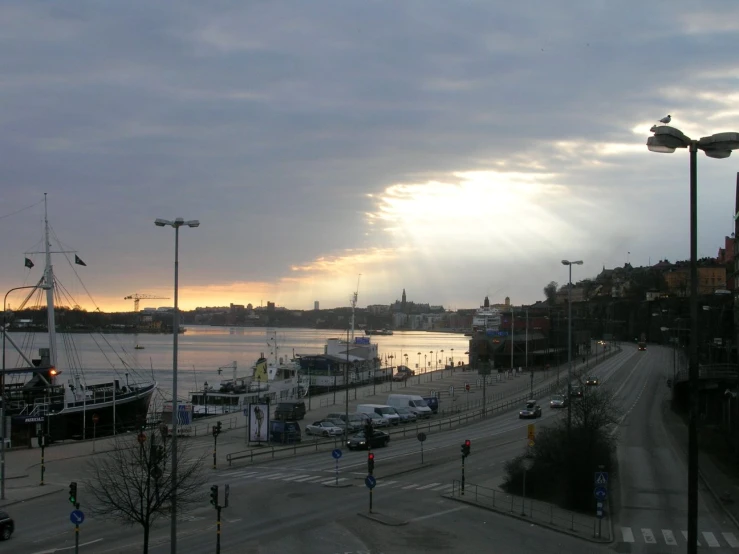 cars drive past the water with boats at sunset