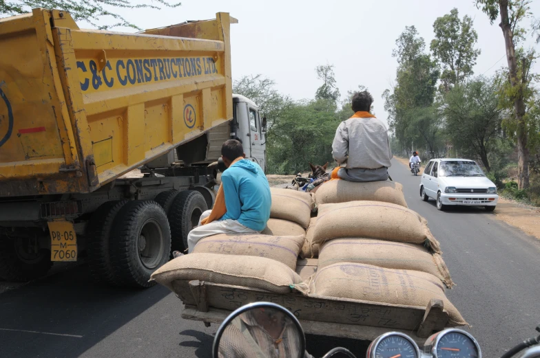 two people sitting on top of a large truck with sandbags strapped to it