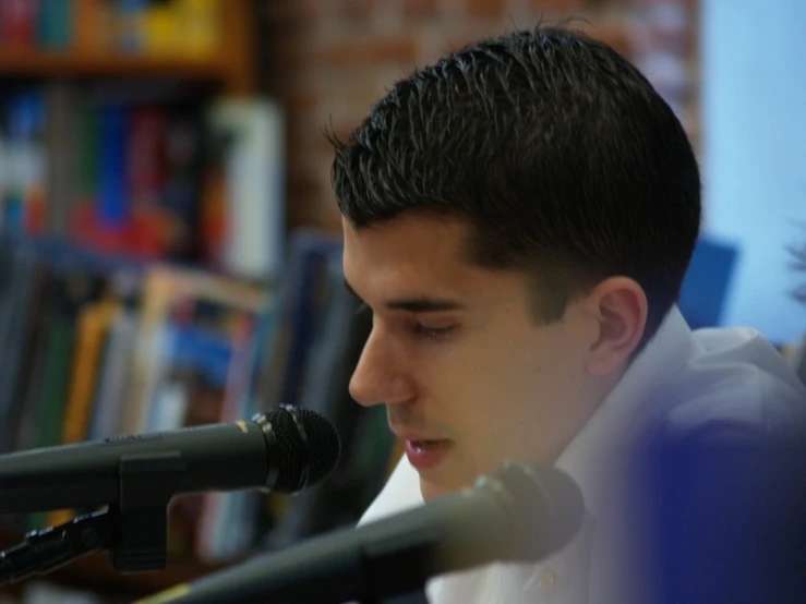 young man reading at microphone with books behind him