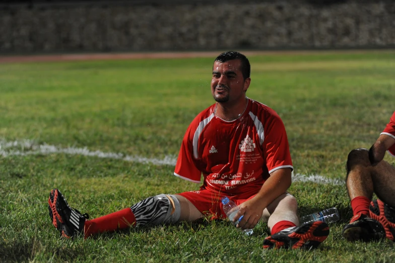 a man is sitting on the grass wearing a red shirt