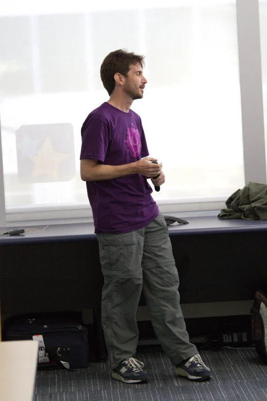 a man in a purple shirt standing near a window