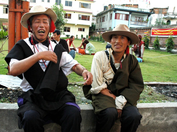 two men wearing hats sit on the concrete edge of a park