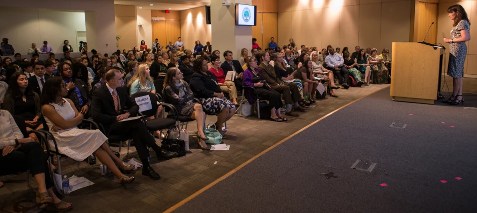 an audience watches as a woman speaks at the podium