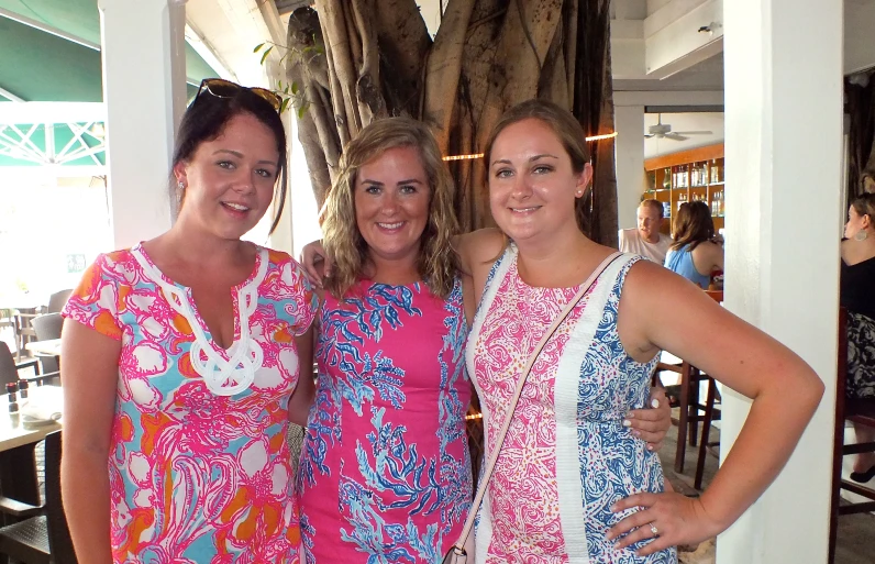 three women wearing colorful dresses stand together in front of a table