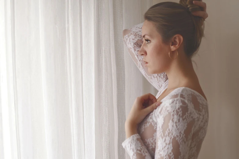 a woman standing near a window with an open white curtain