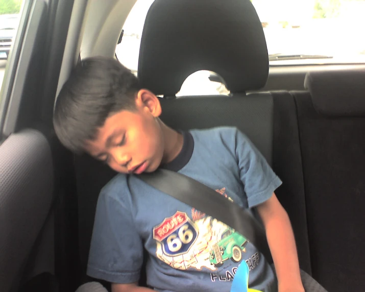 a child sleeping in a car with his head resting on the seat belt