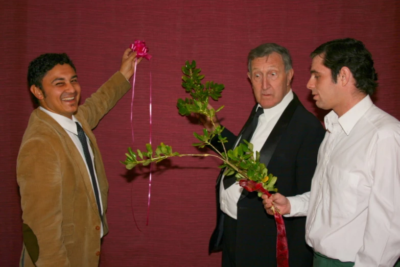 three men in suits holding up plants