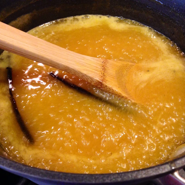 a wooden spoon stirring liquid into an oil in a pot
