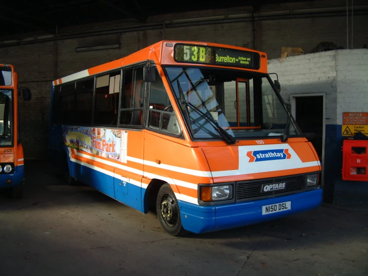 two buses parked in a garage while one is blue and orange