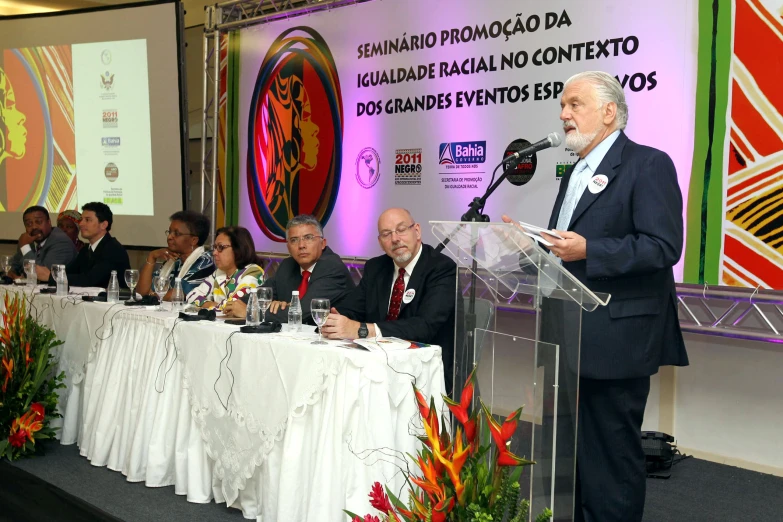 several people sitting at a table listening to speakers