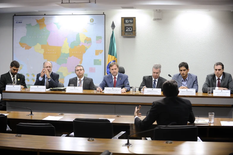 four men sitting at desks in front of a map