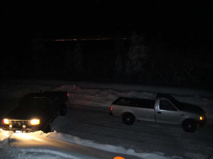 two cars parked on a snowy road at night