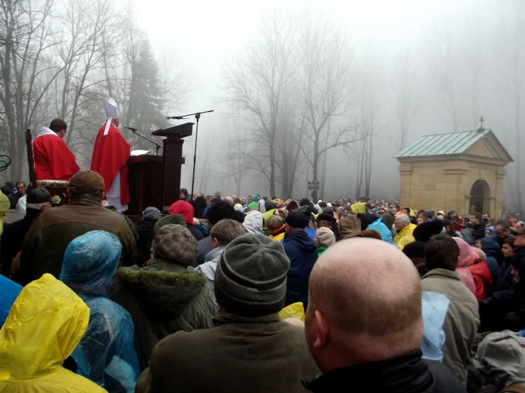 people are sitting in the fog as two priests sing