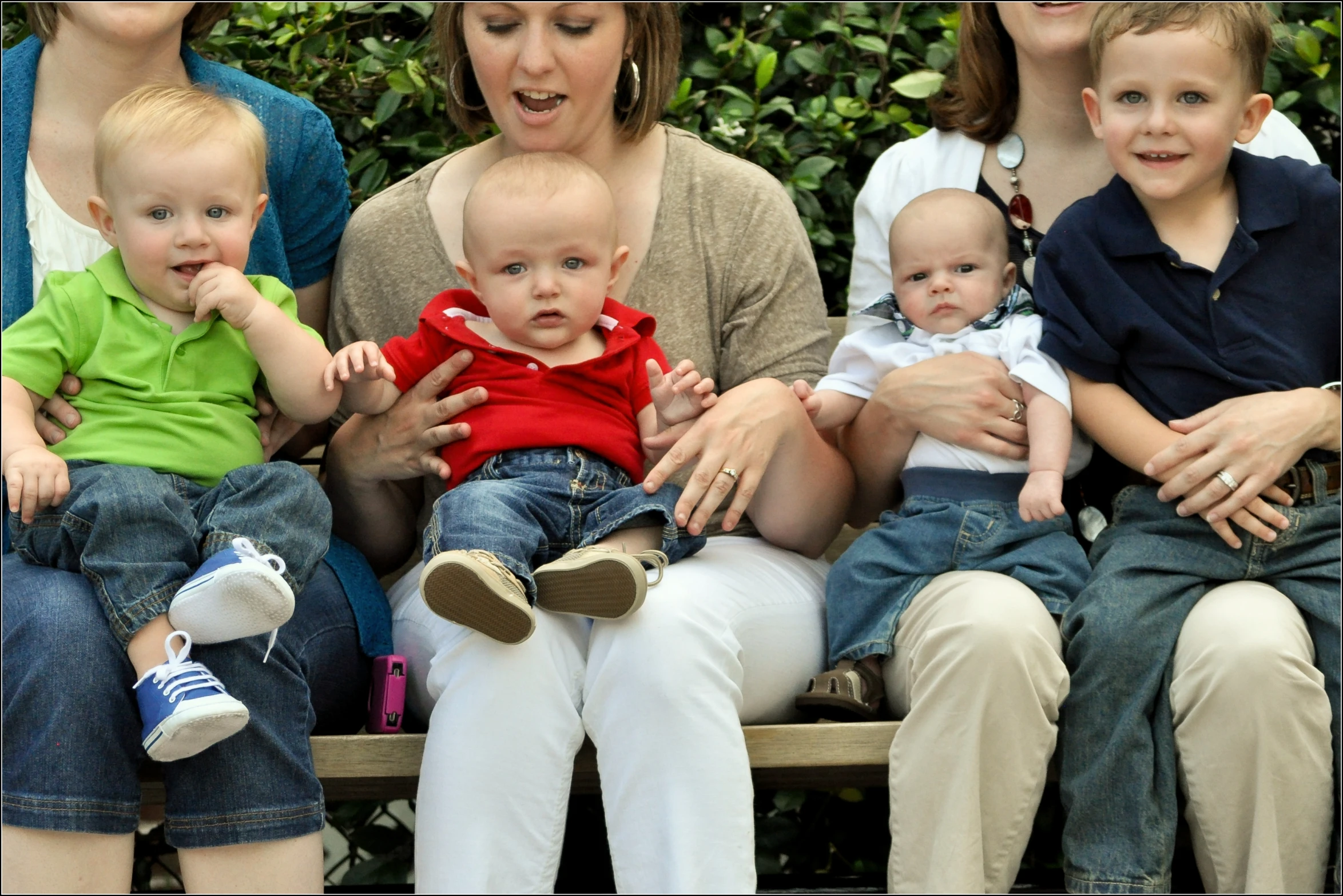 there are people sitting on a bench and one woman holding two babies