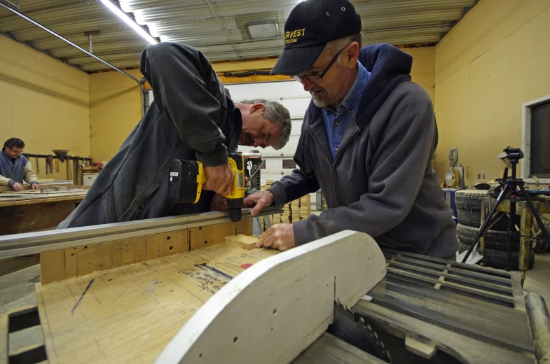 two men in a factory using a saw to cut wooden items