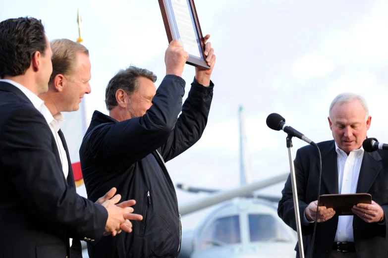 three men with microphones are holding up a plaque