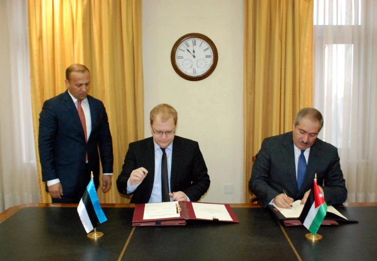 three men at table signing papers with flags