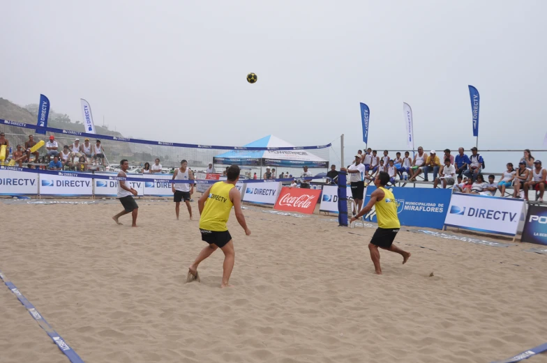 men playing beach volleyball on the beach in a crowded arena