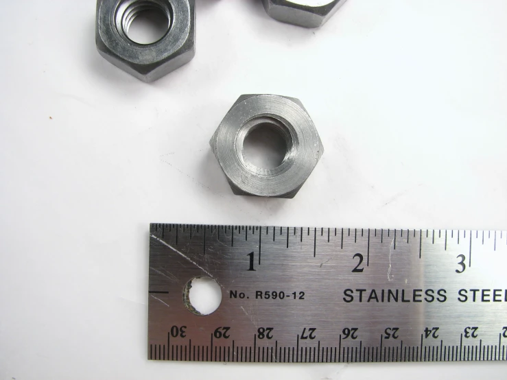 two small metal nuts sitting next to a ruler