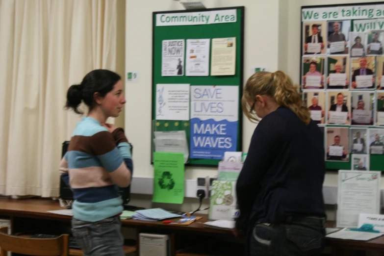 two women standing in front of a desk with a laptop on it