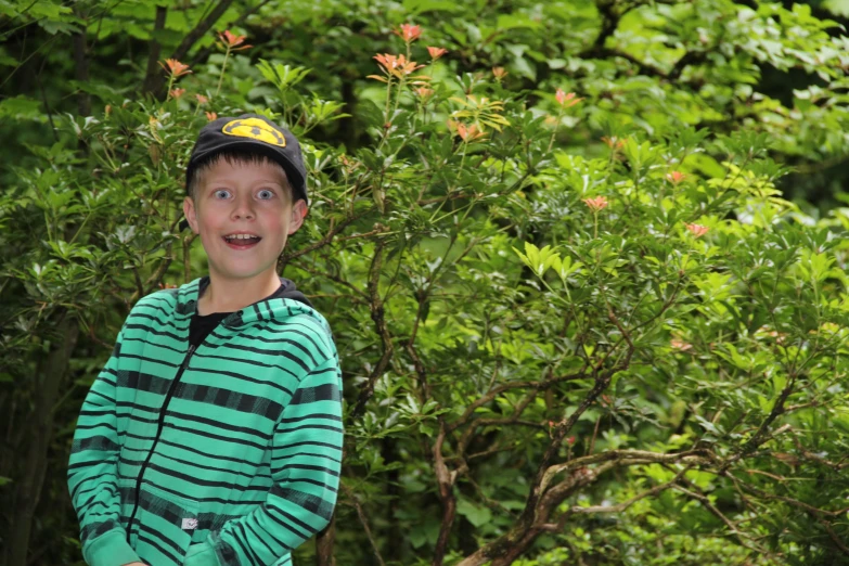 the boy is standing in front of a bush with trees in the background