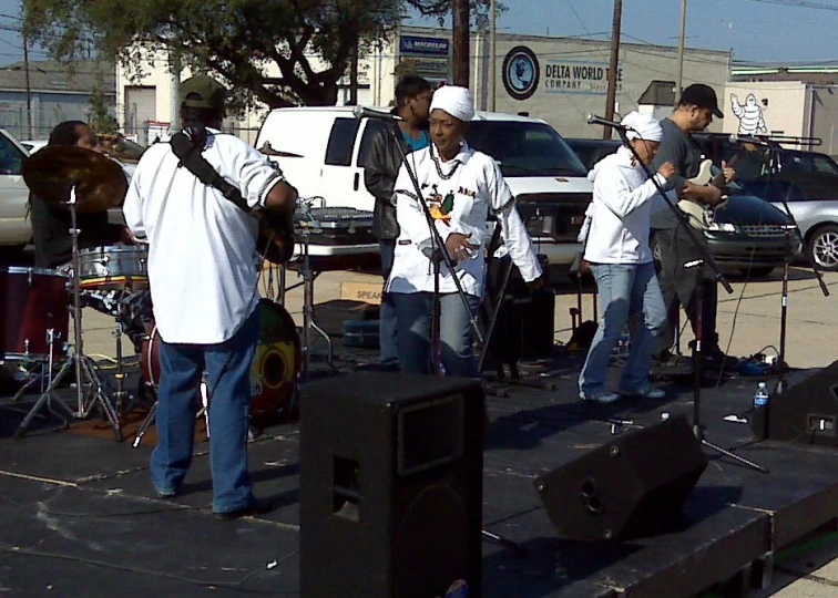 four men on stage playing instruments near some cars
