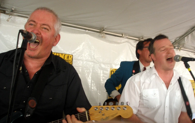 two men play guitar in front of a microphone and sing