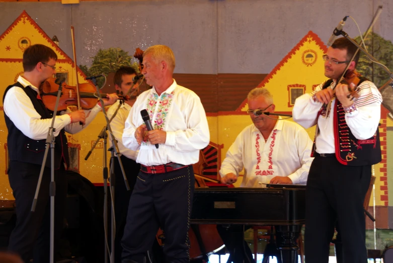 two men wearing colorful vests playing musical instruments while others stand in the background