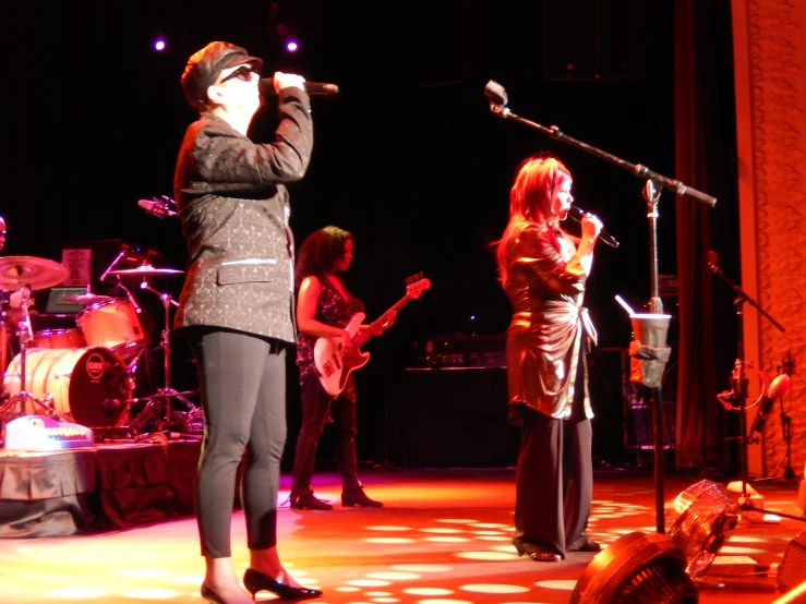 a woman on stage singing into a microphone with two men