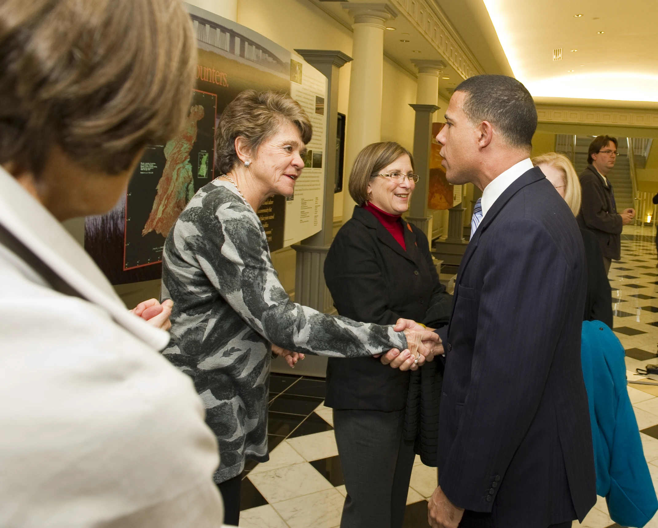 three people shaking hands as others walk by in a hallway