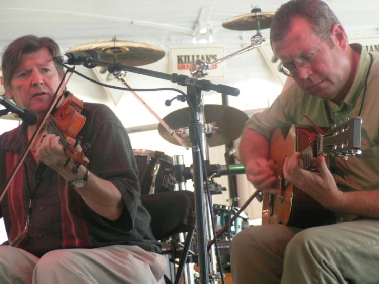 a man in glasses is playing on a violin while another plays a guitar