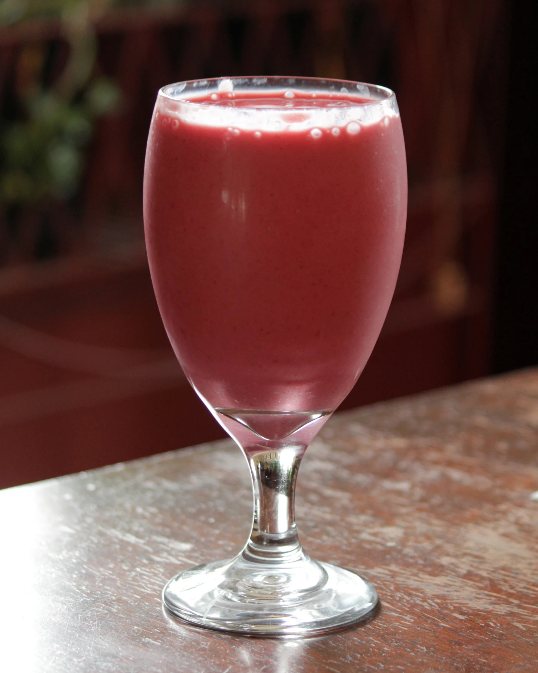 a red drink in a glass sitting on top of a wooden table