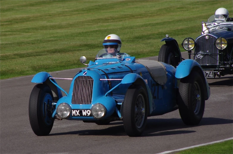 two old cars driving around a track at an event