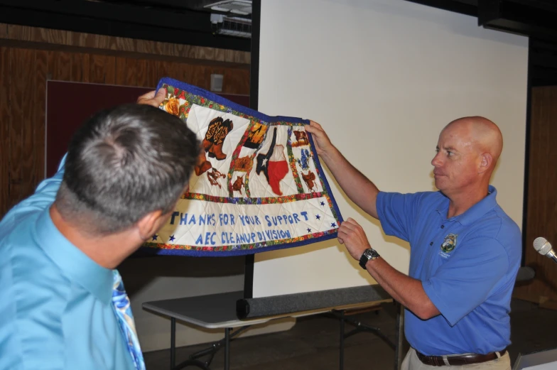 two men holding a colorful cloth with an image of women and children