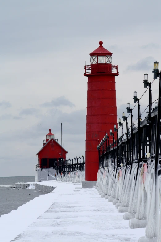 a red light house sitting on top of a snow covered pier