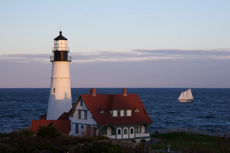 the white and red lighthouse is beside a sailboat