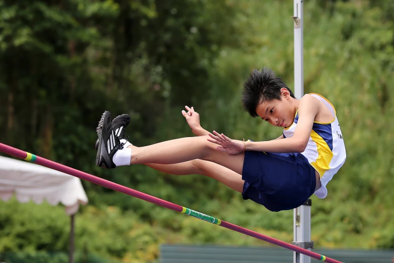 boy with shirt tied to knee jumping high in track and field