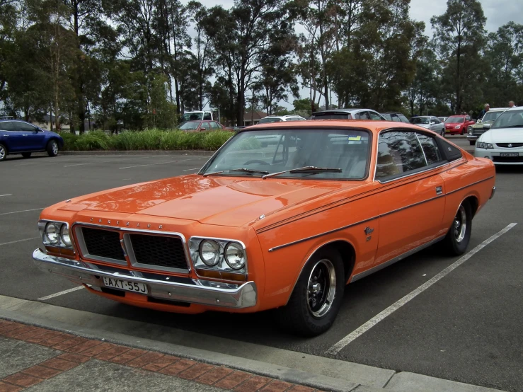 an orange mustang parked in a lot near other cars