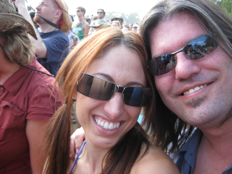 a couple with sunglasses smiling in front of people