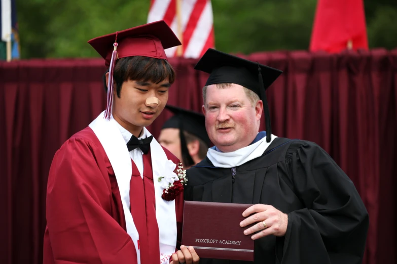 two graduates stand near each other, one is in his graduation gown and the other is in his graduation gown