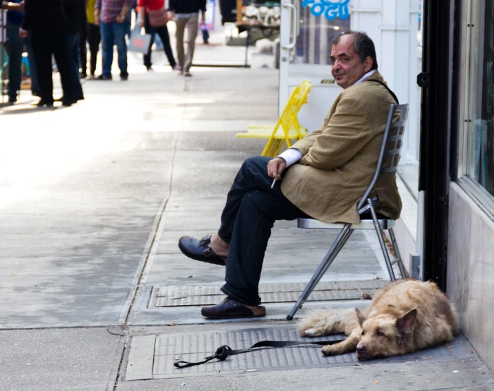 the man is sitting on a chair outside next to his dog