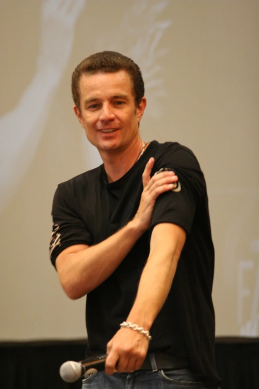 a man in a black t - shirt standing with his hands on his chest