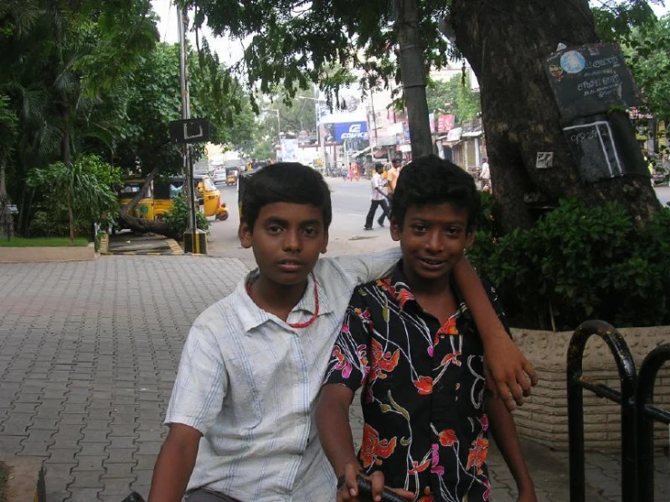 two boys sitting next to each other on a city street