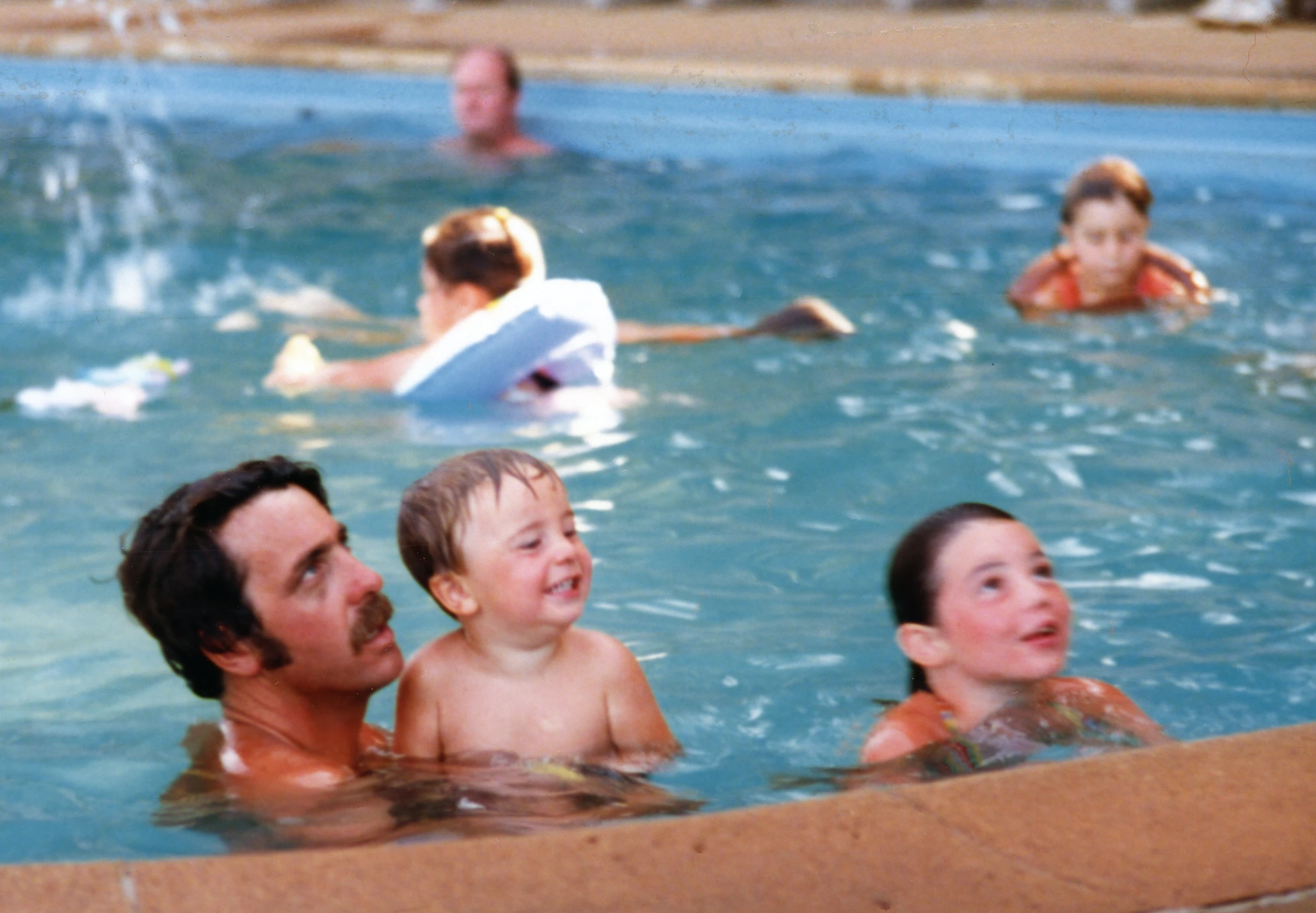 many adults and children swimming in a large swimming pool