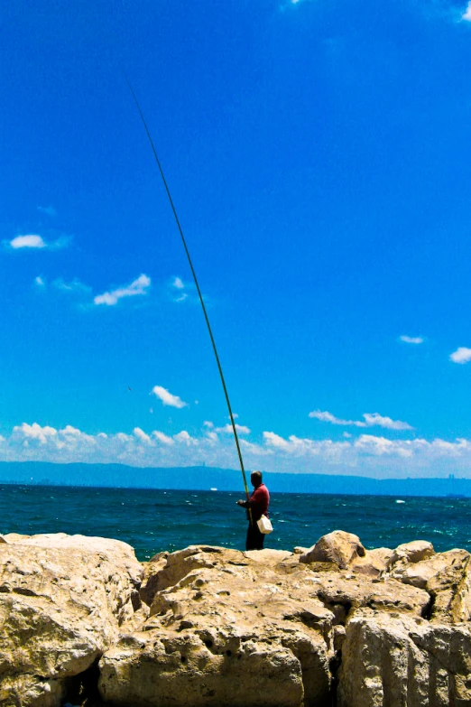 a man stands on a rock and flies a fishing pole