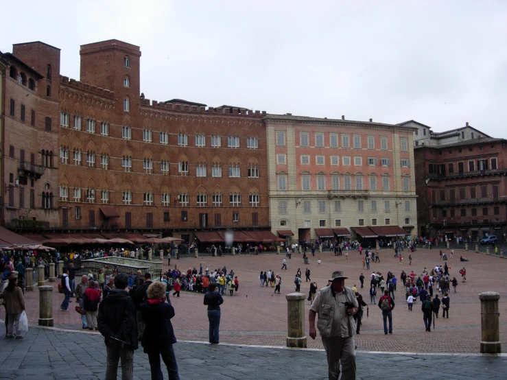 people walk around and around an area that includes tall buildings, a plaza with two sides where several people are on and out