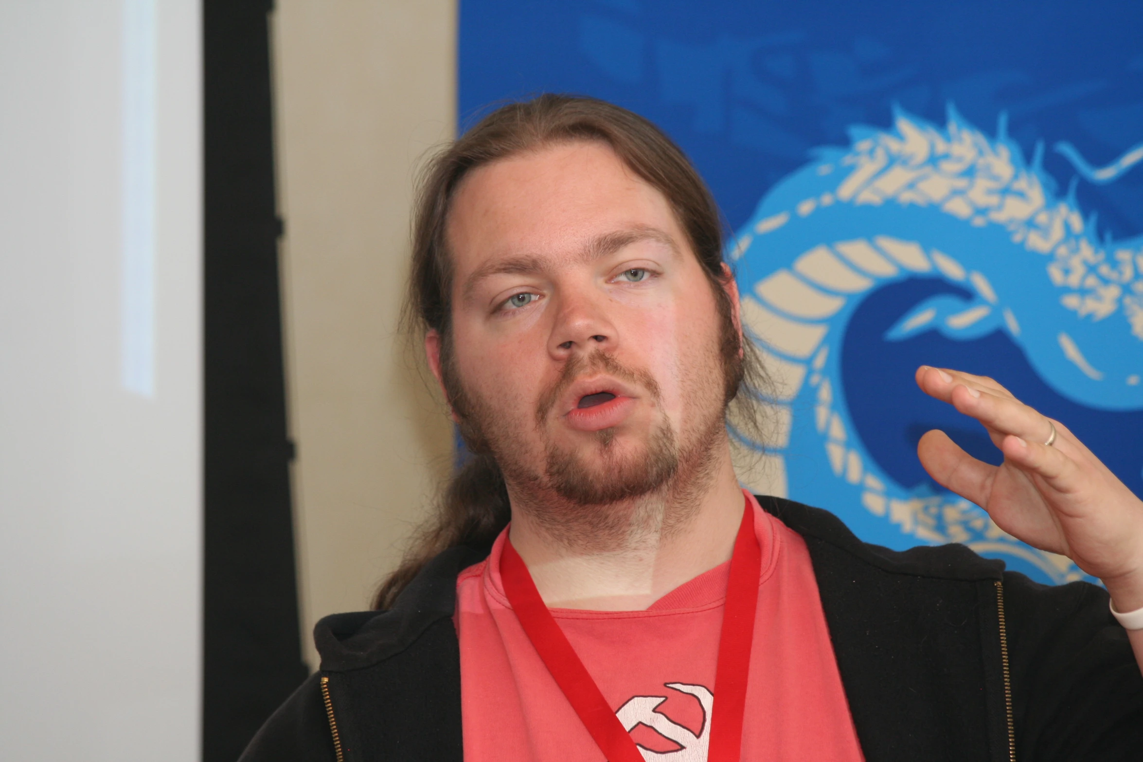 man with open arms giving speech while standing in front of a dragon sign